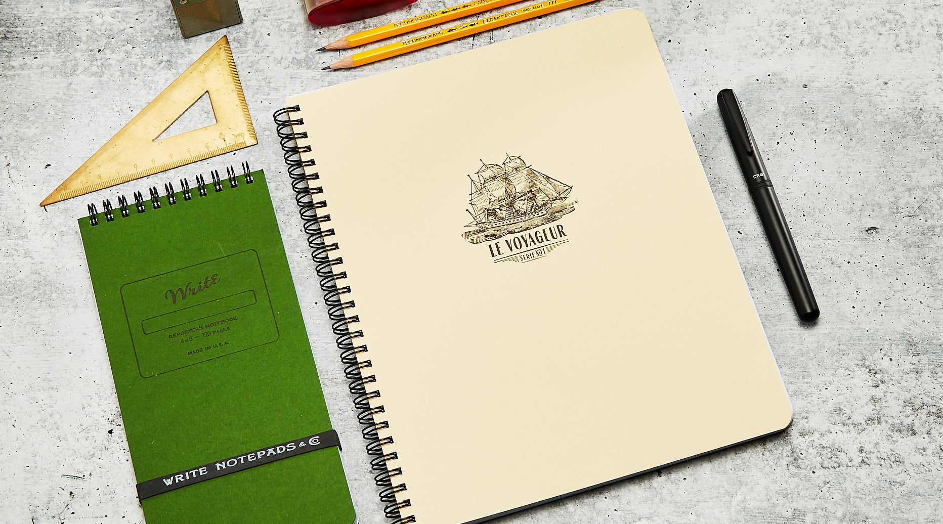 Le Voyageur limited edition notebook on table with a forest colored Reporter notebook next to it and a pen to the right