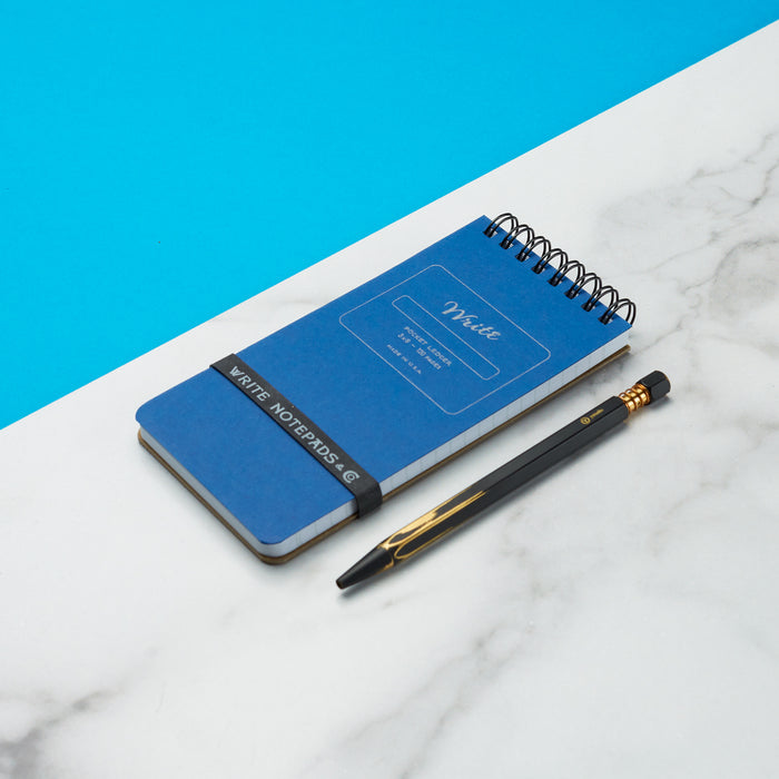 Blue pocket ledger notebook with a spiral top binding, labeled 'Write' on a white and blue contrasting background. A sleek black pen with gold accents lies adjacent.